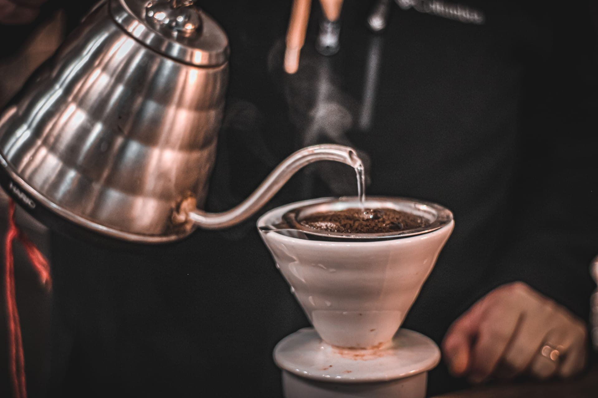 A gooseneck kettle pouring a thin stream of water into a coffee dripper